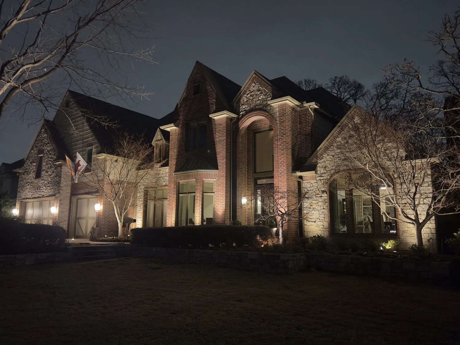 A brick and stone Tulsa home with the gables and planting lit at night