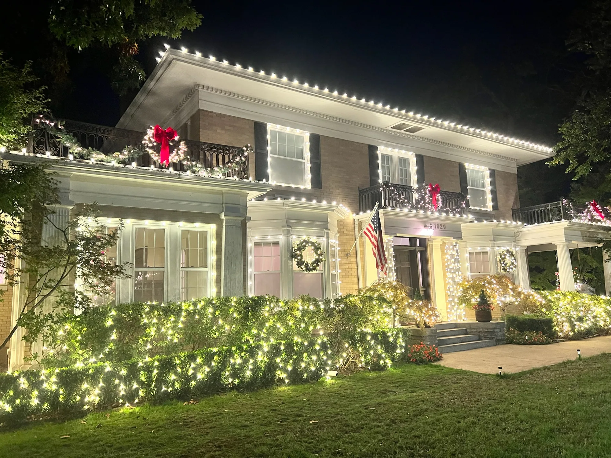 Wreaths, bows and lit hedges on a colonial. Christmas Lighting by LIT Outdoor Lighting in Tulsa.