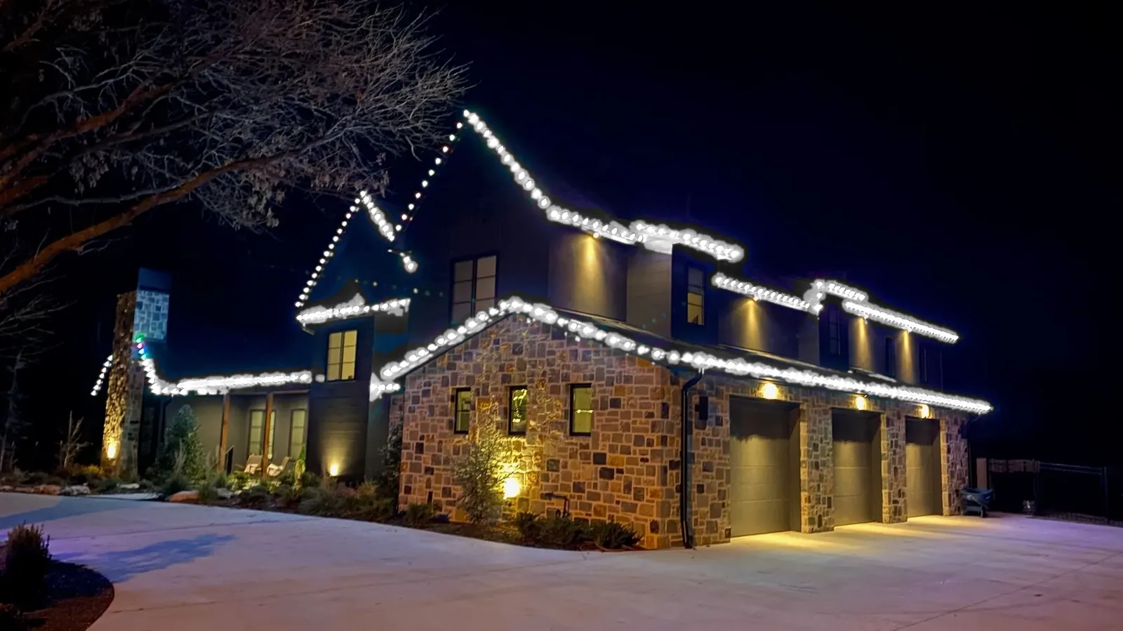 A stone and board-and-batten home at night with permanent lighting along every roofline