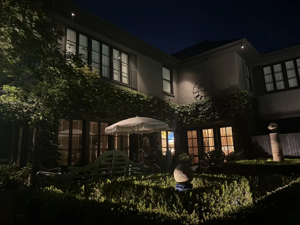 Back garden and glass-walled home lit after dark. Landscape Lighting by LIT Outdoor Lighting in Tulsa.