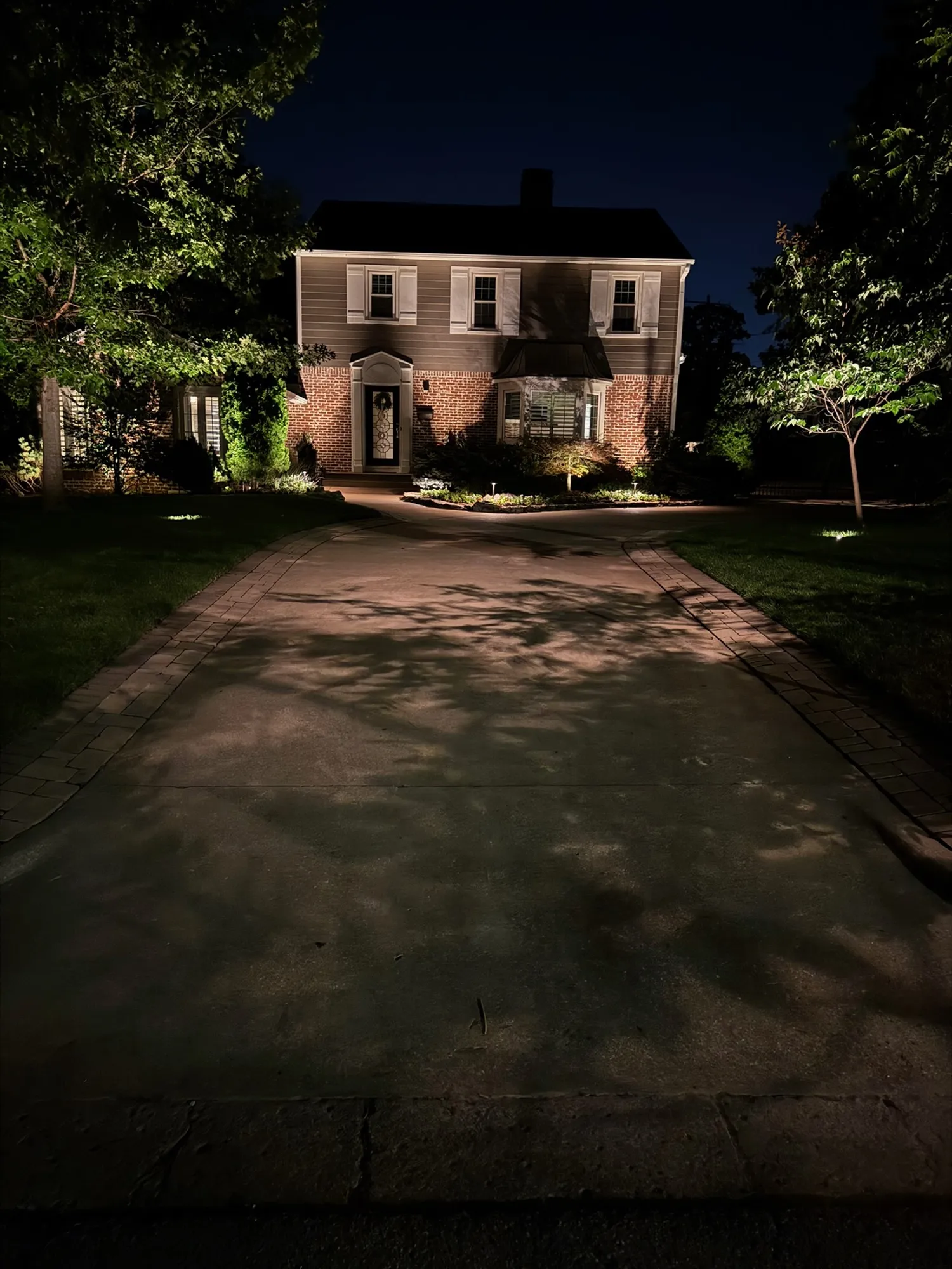 Brick home framed by lit trees at the end of the drive. Landscape Lighting by LIT Outdoor Lighting in Tulsa.