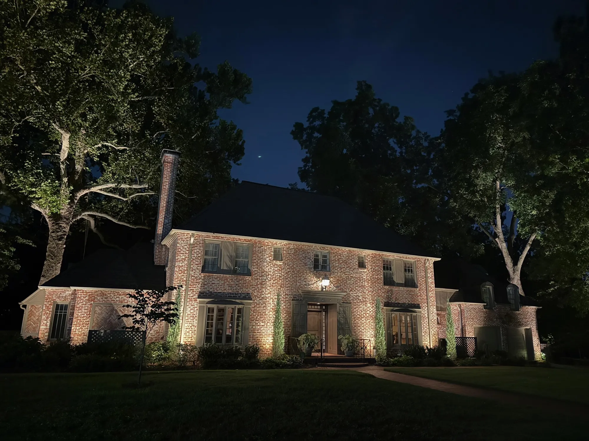 Brick home under lit oaks. Landscape Lighting by LIT Outdoor Lighting in Tulsa.