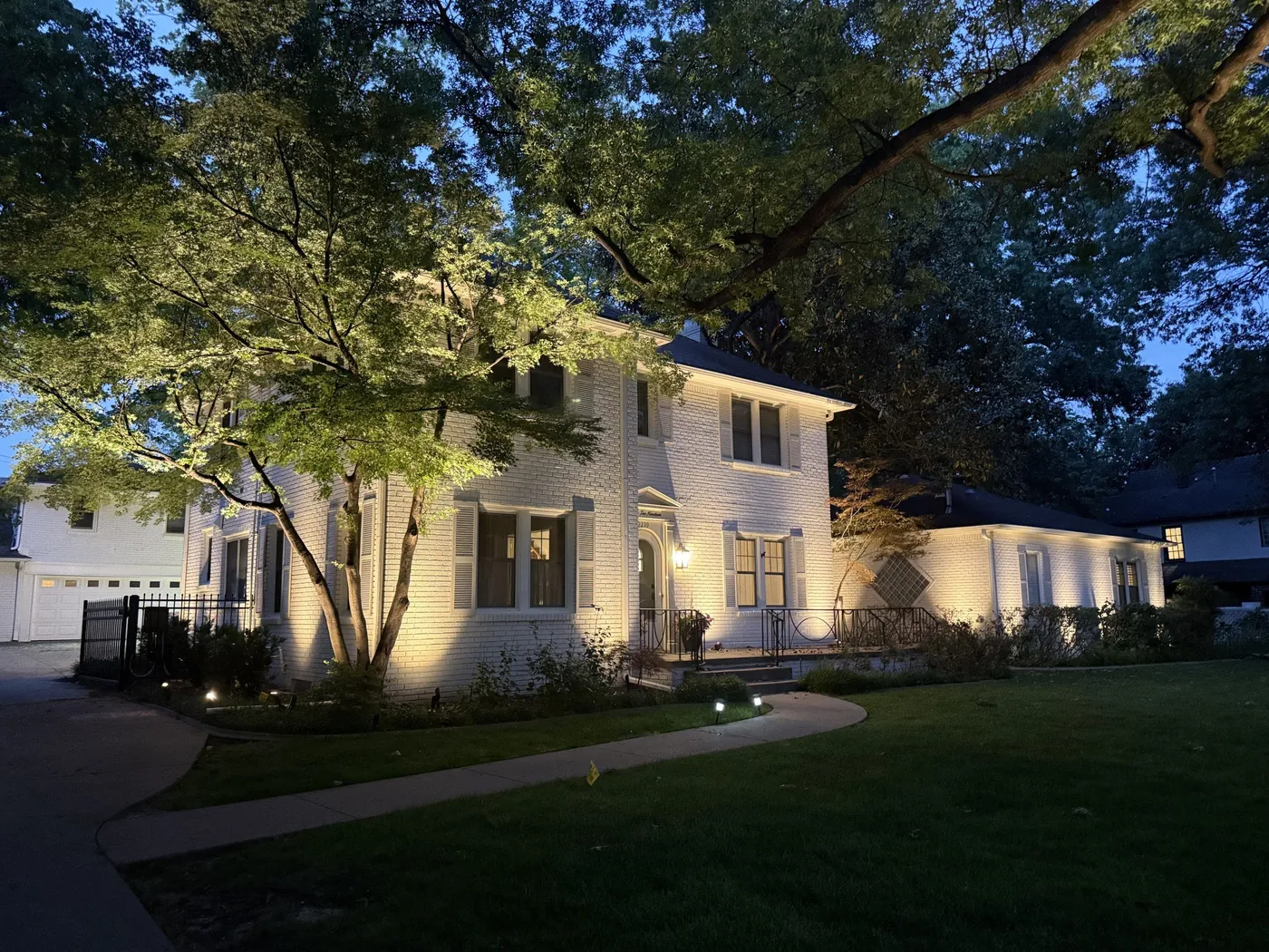 A white brick home in Tulsa with the trees and facade uplit at night