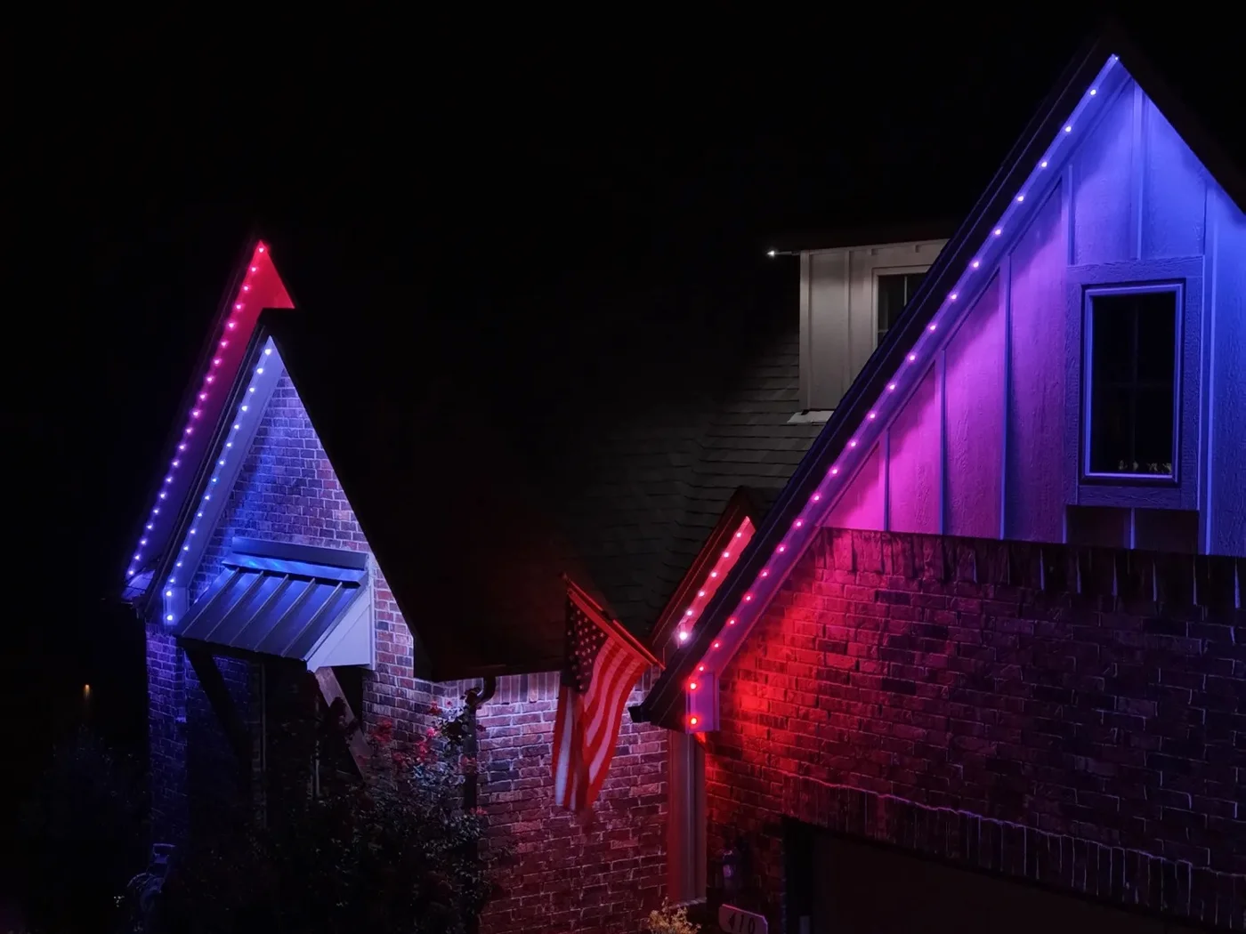 Permanent roofline lighting on two brick gables at night, running red, white and blue