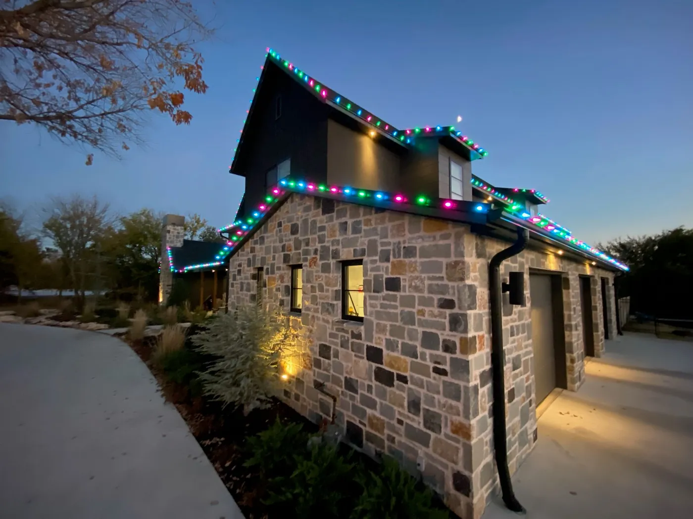 Stone home with a multicolour roofline at dusk. Christmas Lighting by LIT Outdoor Lighting in Tulsa.